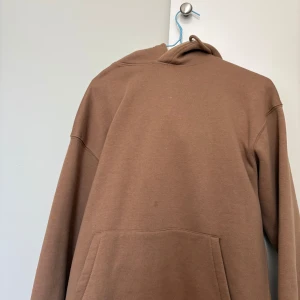 Brun hoodie med magficka - Säljer en enkel brun hoodie med huva och stor magficka framtill. Tröjan har långa ärmar och en avslappnad passform, perfekt för vardagsbruk. Passar dig som gillar basic och stilrena plagg.