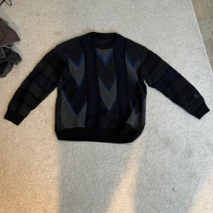Vintage Mörkblå och grå stickad tröja med mönster - Säljer en stickad tröja i mörkblått och grått med coolt geometriskt mönster framtill. Tröjan har rund halsringning och långa ärmar. 