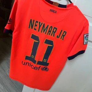 FC Barcelona Neymar Jr 11 matchtröja - Säljer en orange FC Barcelona fotbollströja med Neymar Jr och nummer 11 på ryggen. Tröjan har korta ärmar, mörkblå detaljer och LFP-märke på ärmen. Qatar Airways-logga på bröstet och klubbmärke. Perfekt för fans av Barça och Neymar! Vet inte om den är äkta 