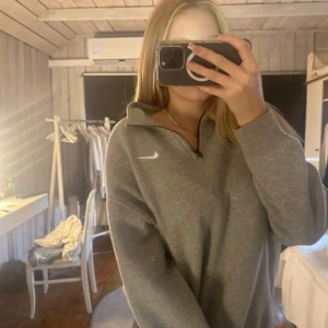 Grå halvzip sweatshirt från Nike - Säljer en grå sweatshirt från Nike med halv dragkedja och hög krage. Tröjan har lång ärm och en enkel, stilren design med Nike-logga på bröstet. Perfekt för en avslappnad och sportig look.