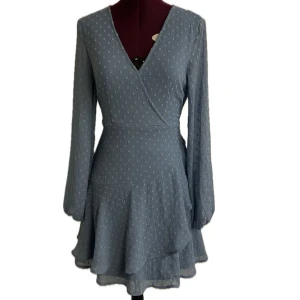 Blå långärmad miniklänning med v-rigning och knyt i ryggen. - Gullig blå klänning med v-rigning, långa ärmar och flera volanger. Materialet är tunnt och luftigt och lätt genomskinligt vid ärmarna. Det kommer även med ett band som kan knytas antingen bak, fram eller runt midjan. Endast använd en gång! 