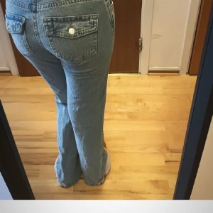 Lågmidjade jeans med knappar - Säljer ett par klassiska blå jeans med låg midja och raka, lite lösare ben. Jeansen har knappar på bakfickorna och en tidlös denimlook som passar till det mesta. 