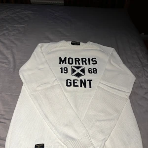 Vit stickad tröja från Morris Gents - Säljer en vit stickad tröja från Morris Gents med svart tryck på framsidan: 'Morris 1968 Gent'. Tröjan har långa ärmar och ribbade muddar vid ärmslut och nederkant. Klassisk och stilren design, Storlek L men passar även storlek M. Öppen för prisförslag!