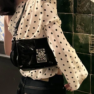  DKNY väska - Säljer en svart axelväska från DKNY. Väskan har ett silvrigt lås framtill, justerbar axelrem och innerfack med dragkedja!