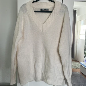 Vit stickad v-ringad tröja från F2 Sister - Mysig vit stickad tröja från F2 Sister med djup v-ringning och långa ärmar. Perfekt för lager-på-lager och passar till både jeans och kjol. Tröjan har bred ribbad kant vid hals, ärmslut och nederkant. Bak på tröjan finns det en fläck.