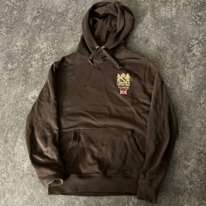 Brun hoodie från Morris - Säljer en brun hoodie från Morris med broderad logga och brittisk flagga på bröstet. Perfekt för en avslappnad stil.