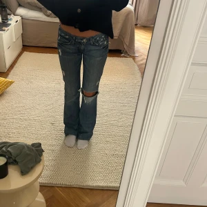 7 all mainkind jeans - Säljer ett par blå bootcut jeans med slitning och stort hål på ena knät. Från Seven all mainkind, uppskattad storlek:36, jag är 178, midjemått:39, innebenslängd:88