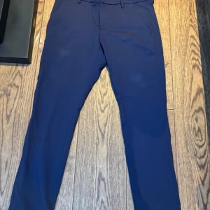 Mörkblå kostymbyxor från Dondup - Säljer ett par mörkblå kostymbyxor från Dondup, tillverkade i Italien. Byxorna har normal passform, raka ben och klassiska fickor fram och bak. Perfekta för en stilren och dressad look.