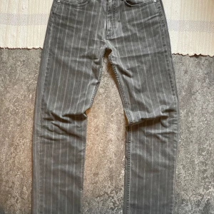 Gråa randiga jeansbyxor från Lee Cooper - Säljer ett par gråa jeansbyxor från Lee Cooper med tunna vita ränder. Klassisk femficksmodell med knapp och dragkedja i gylfen. Snyggt Lee Cooper-märke på bakfickan och läderpatch i midjan. Perfekta för dig som vill ha en stilren look.