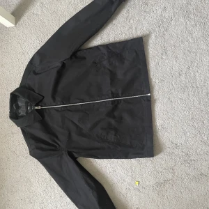 Svart jacka från ASOS DESIGN - Säljer en stilren svart jacka från ASOS DESIGN med dragkedja framtill och klassisk krage. Jackan har långa ärmar och snedställda fickor. Perfekt för dig som gillar enkel och tidlös stil.