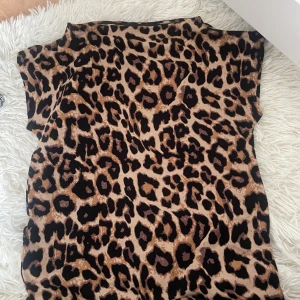 Leopardmönstrad topp från The Black Label Collection - Säljer en snygg leopardmönstrad topp från The Black Label Collection. Toppen har en lös passform och är ärmlös, perfekt för att sticka ut med ett djurmönster. Färgerna går i beige, brunt och svart.