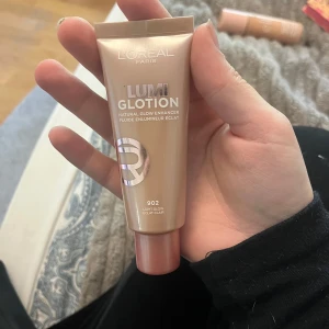 L'Oréal Paris Lumi Glotion 902 Light Glow - Ljusreflekterande highlighter i flytande form från L'Oréal Paris. Nyansen är 902 Light Glow, perfekt för att ge huden en naturlig lyster. Kommer i en beige-rosa tub med skruvkork och metallisk text. Aldrig använd 