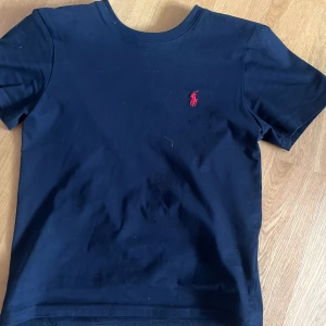 Svart t-shirt från Polo Ralph Lauren - En svart Ralph lauren t shirt med rött märke, den ser blå ut men är svart. Pris kan diskuteras