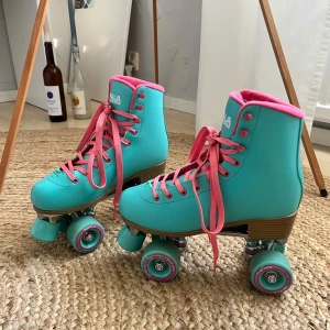 Turkosa rullskridskor från Impala med rosa detaljer - Ettt par  turkosa rullskridskor från Impala med rosa snörning och foder. Skorna har klassisk retrostil med högt skaft och robust platt sula. Passar både nybörjare och erfarna åkare. De är knappt använda, men är tvungen till att sälja dessa pga att de är för små för mig