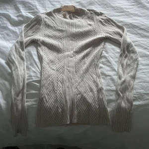 Beige ribbad tröja från H&M - Säljer en beige ribbad långärmad tröja från H&M. Tröjan har en tight passform och är tillverkad i ett mjukt material som sitter skönt mot kroppen. Perfekt att styla med jeans eller kjol för en enkel och stilren look.