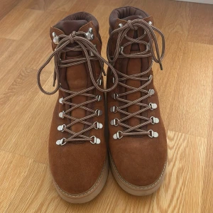 Bruna mockaboots från Face - Säljer ett par bruna boots från Face i mocka med grov beige sula. Skorna har snörning med metallöglor och högre skaft, perfekta för kyligare dagar. Snygg och robust design som passar till många outfits.