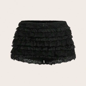 Svarta minishorts med spets - Säljer ett par svarta mini shorts med flera lager volanger och spetsdetaljer. De har en liten rosett framtill och är perfekta för dig som vill ha något extra. Passar till många olika stilar och är riktigt snygga!