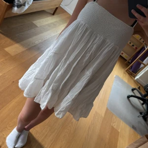 Vit volangklänning med smockliv - Säljer en söt vit klänning med smockat liv och volangig kjol. Klänningen är ärmlös och har en luftig, somrig känsla. Perfekt för varma dagar och enkel att styla med sandaler eller sneakers.
