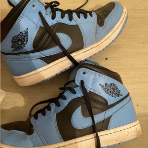 Nike Air Jordan 1 High OG University Blue - Säljer ett par Nike Air Jordan 1 High OG i färgen University Blue. Skorna har svart och ljusblått skinn, klassisk Air Jordan-logga på sidan och svart snörning. Perfekta för dig som gillar streetwear och sneakers med ikonisk design.                                   ( de kommer att rengöras innan de skickas )