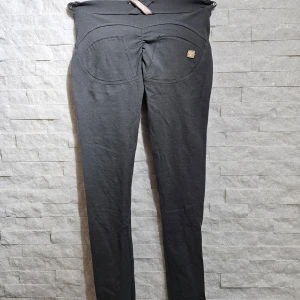 Svarta shapingbyxor från Freddy WR.UP - Säljer ett par svarta shapingbyxor från Freddy WR.UP med hög midja och skinny passform. Byxorna har knappar och dragkedja framtill samt dekorativa sömmar och logga bak. Stretchigt material som formar och lyfter.