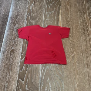Röd t-shirt från Lacoste Sport - Fläckarna som ni ser är vatten.Säljer en röd t-shirt från Lacoste Sport