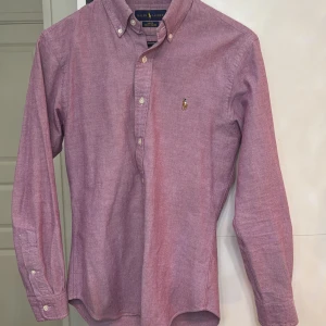 Rosa skjorta från Ralph Lauren - Säljer en stilren rosa skjorta från Ralph Lauren i slim fit. Skjortan har långa ärmar och knappar framtill samt en broderad logotyp på bröstet. Perfekt för en elegant look. Super fin nu till våren/sommaren.
