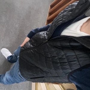 Svart quiltad väst från On Our Terms - Säljer en stilren svart quiltad väst från On Our Terms. Västen har en dragkedja framtill och är perfekt för lager-på-lager under kyligare dagar. Den är lätt och smidig att bära, vilket gör den till ett mångsidigt plagg i garderoben.