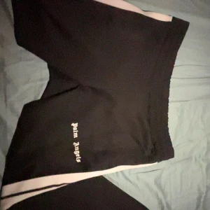 Svarta byxor från Palm Angels - Snygga svarta byxor från Palm Angels med vita sidoremsor. Perfekta för en stilren look. Märkesloggan är tryckt på framsidan. Kommer i original påsen ⚠️pris kan diskuteras⚠️