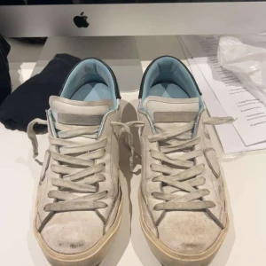 Vita sneakers med blå detaljer - Säljer ett par Philippe modells köpta på sicuro fashion box och kvitto följer med. finns lite defekter på sulan och även ett snöre gått sönder lite. Priset kan diskuteras.