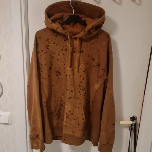 Brun hoodie från Supreme - Säljer en brun hoodie från Supreme med ett unikt stänkmönster. Hoodien har en stor ficka framtill och en broderad logga på huvan. Tillverkad i 100% bomull och gjord i Kanada. Perfekt för en avslappnad stil.