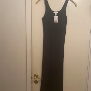 Svart ärmlös långklänning - Snygg svart långklänning med ärmlös design och rund halsringning. Perfekt för en stilren look. Klänningen är figurnära och passar utmärkt till olika tillfällen.