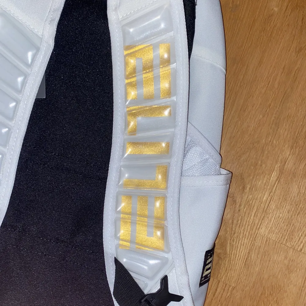 Snygg ryggsäck från Nike i vit och svart med guldiga detaljer. Ryggsäcken har flera fack och justerbara axelremmar. Perfekt för både träning och vardag. Märket 'ELITE' syns tydligt på baksidan.. Laukut & Käsilaukut.
