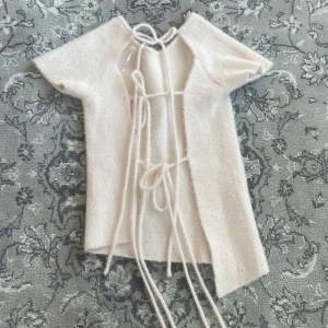 Beige kortärmad topp från Zara - Säljer en helt ny stilren beige topp från Zara i s med korta ärmar och unik snörning bak. Toppen har en asymmetrisk design och är tillverkad i ett mjukt material.