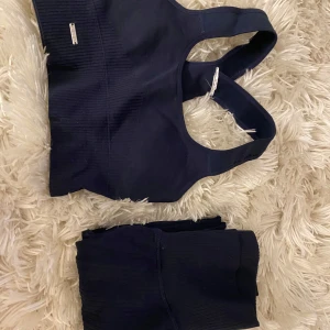 Mörkblå ribbad sportset - Säljer en mörkblå ribbad sporttopp med breda axelband och byxor en stilren design. Perfekt för träning eller en aktiv vardag. Settet har en bekväm passform och är tillverkad i ett stretchigt material.