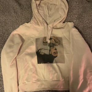 Ariana Grande tröja  - Säljer en vit hoodie med en stor bildtryck på framsidan. Hoodien har en klassisk design med dragsko i huvan och ribbade muddar vid ärmslut och nederkant. Perfekt för en avslappnad stil.