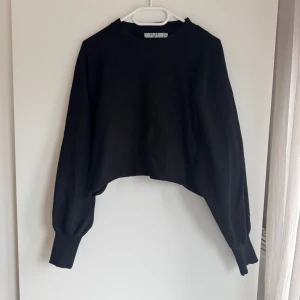Svart croppad tröja från NA-KD - Säljer en stilren svart croppad tröja från NA-KD. Tröjan har långa ärmar och en ribbad rund halsringning. Perfekt för en trendig look.