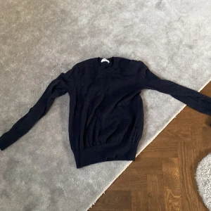 Mörkblå tröja från Filippa K - Säljer en stilren mörkblå tröja från Filippa K. Tröjan har en klassisk design med långa ärmar och rund halsringning. Perfekt för en minimalistisk garderob.