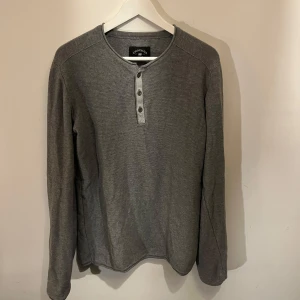 Grå långärmad tröja med knappar - Säljer en stilren grå långärmad tröja från  crocker . Tröjan har en knappslå med tre knappar framtill och en rund halsringning. Perfekt för en avslappnad look.