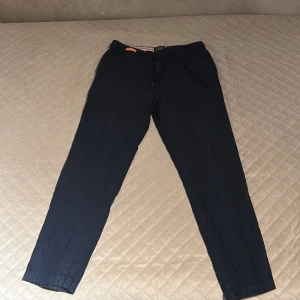 Mörkblå byxor från Scotch & Soda - Snygga mörkblå byxor från Scotch & Soda med en avslappnad passform. Perfekta för en stilren och bekväm look. Byxorna har en elastisk midja med snörning för extra komfort.