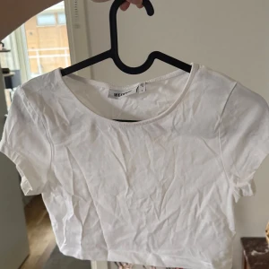Vit croppad topp från Weekday - Säljer en stilren vit croppad topp från Weekday. Perfekt för varma dagar med sin enkla design och korta passform. Toppen har en rund halsringning och korta ärmar. Passar perfekt till jeans eller kjol för en avslappnad look.