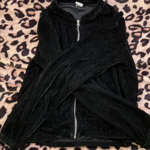 Svart sammet kofta med dragkedja - Säljer en svart sammet kofta med dragkedja framtill. Koftan har långa ärmar och en mjuk, glansig yta som ger en lyxig känsla. Perfekt för att lägga till en touch av glamour till din outfit. Är storlek 146/152 passar även mig som kan ha xs i vissa kläder