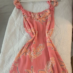Rosa blommig klänning, inför sommaren - Säljer en söt rosa klänning med blommigt mönster. Klänningen har volangdetaljer vid axelbanden och en luftig passform. Perfekt för sommarens varma dagar!
