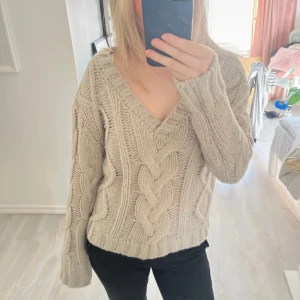 Beige stickad tröja med flätmönster - Mysig beige stickad tröja med ett snyggt flätmönster och v-ringad hals. Perfekt för kyligare dagar. Tröjan har långa ärmar och en avslappnad passform. Använd en gång 