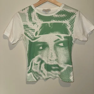 Vit och grön t-shirt med grafiskt tryck - Säljer min vita t-shirt med ett stort grönt grafiskt tryck av ett ansikte. Toppen har en ganska kort passform så jag skickar gärna fler bilder privat!💗