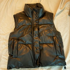 Svart dunväst från Zara - Snygg svart väst från Zara med hög krage och knappar framtill. Perfekt för kyliga vår dagar när du vill hålla stilen. Västen har en modern look och är lätt att matcha med olika outfits. Ursprungspris 599kr