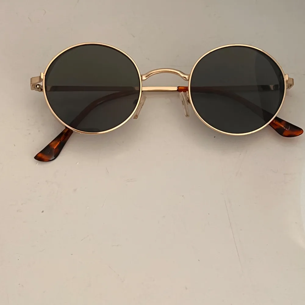 Snygga runda solglasögon med guldfärgad metallram och mörka linser. Skalmarna har en cool sköldpaddsmönstrad design som ger en retro känsla. Perfekta för en stilren look.. Muu.