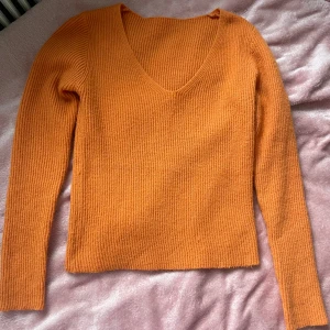 Orange mysig stickad tröja - Säljer en snygg orange stickad tröja med v-ringning. Tröjan har långa ärmar och en ribbad struktur som ger en skön passform. Perfekt för att lysa upp garderoben!🧡 den är figurnära och stretchig passar S-M
