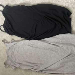 2-pack långa/korta klänningar från SHEIN - Två enkla och stilrena långklänningar från SHEIN i storlek 12Y. En är helsvart och den andra är ljusgrå, båda med smala axelband och rak passform. Perfekta för en chill och avslappnad look. Materialet känns mjukt och stretchigt, troligen bomull eller polyester. Klänningarna går ungefär ner till knäna på mig som är 1,53cm.