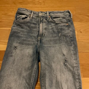 Ljusblå slitna jeans straight fit - Säljer ett par ljusblå jeans med slitningar och distressed detaljer på benen. Klassisk femficksmodell med raka ben och normal passform. Jeansen har en avslappnad vibe och är perfekta för en casual streetstil.