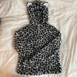 Leopardmönstrad teddyjacka från H&M - Supermjuk teddyjacka från H&M med leopardmönster i svart, brun och beige. Jackan har huva med söta öron och dragkedja framtill. Perfekt för dig som vill sticka ut och hålla dig varm med stil 🫶🫶